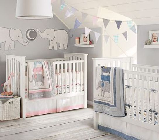 a neutral shared nursery with grey walls, white furniture, paper buntings and decorations, blue and pink bedding to accent each space