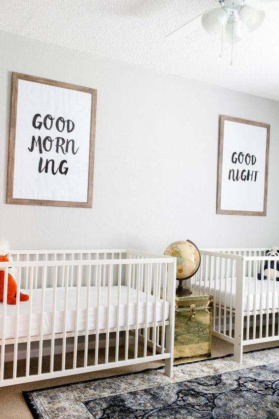 a gender neutral shared nursery with a printed rug, neutral beds, graphic artworks and a gold chest with a globe on it