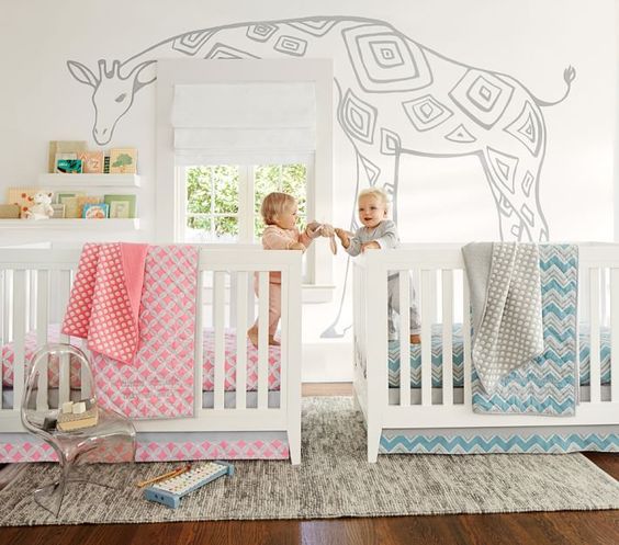 a neutral shared nursery with a fun giraffe on the wall, bookshelves and pink and blue linens to differentiate the boy and the girl zone