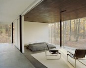 a minimalist bedroom with a mattress on the floor, some chairs and a glass wall with a forest view is veyr calming and peaceful