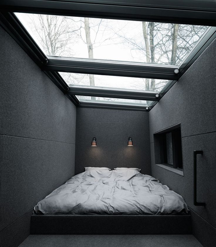 a moody dark bedroom with only a bed on the floor, some sconces, a niche and a glazed ceiling to mazximize daylight in here and look at the stars