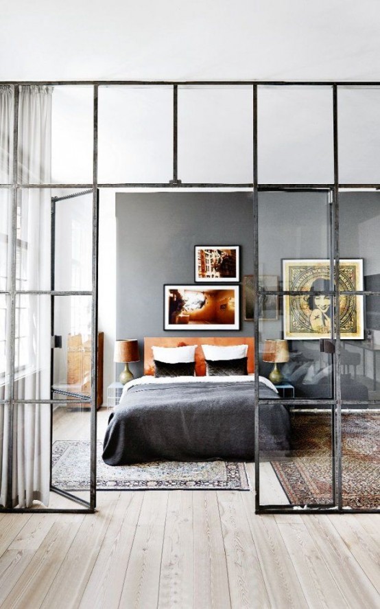 a stylish eclectic bedroom with a grey statement wall, a leather upholstered bed, nightstands and boho rugs plus a framed glass wall that divides the bedroom from the rest of the space