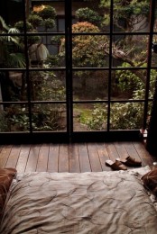 a simple and peaceful zen bedroom with a bed on the floor and a framed glass wall with a gorgeous view to a Japanese garden