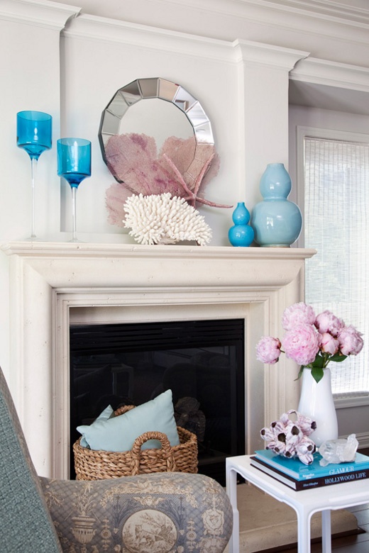a beach mantel with blue glasses and vases, corals and starfish and a large geometric mirror