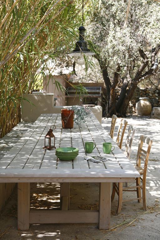 a relaxed Mediterranean dining space outdoors, a long whitewashed table and whitewashed chairs and benches, a pendant lamp on a tree over the tree