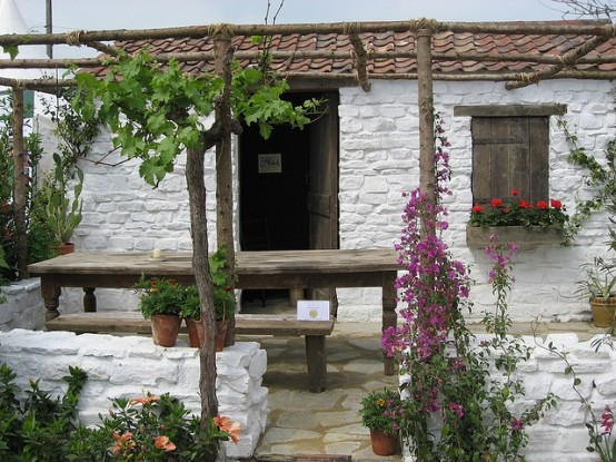 a simple and relaxed Mediterranean outdoor space with white stone walls, lots of greenery and blooms and some simple wooden furniture