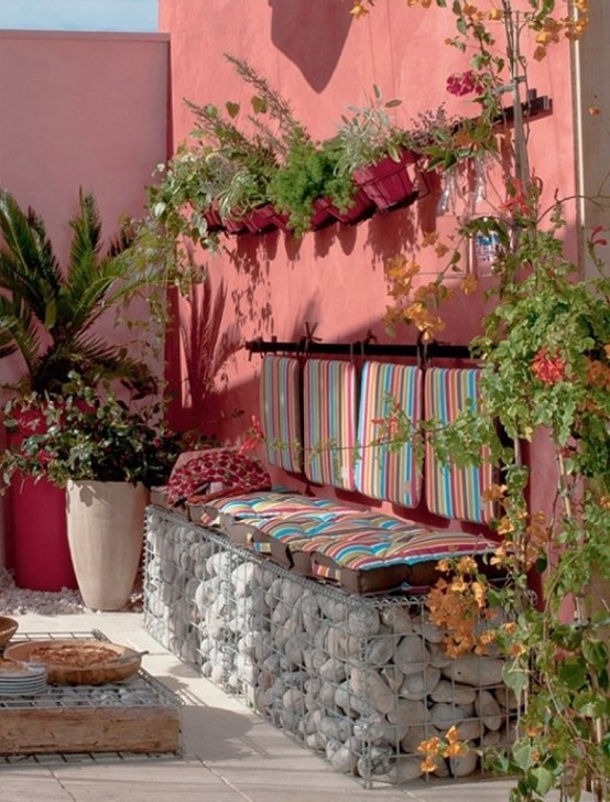 a bright outdoor Mediterranean space with a coral wall, a built-in bench with pebbles inside, bright striped upholstery and lots of greenery around is very atmospheric
