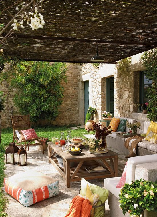 a welcoming Mediterranean outdoor space with a neutral sofa with bright pillows, a stained wooden table, greenery and blooms and candle lanterns is amazing