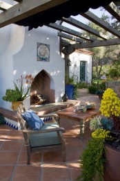 an outdoor Mediterranean living room with a large fireplace, a vintage table and a chair, blooms and bright azulejo tiles on the fireplace