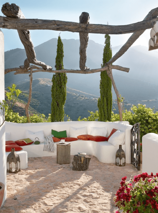 a Mediterranean to Moroccan outdoor space with a white built-in bench, colorful and white pillows, stumps, Moroccan lanterns, blooms