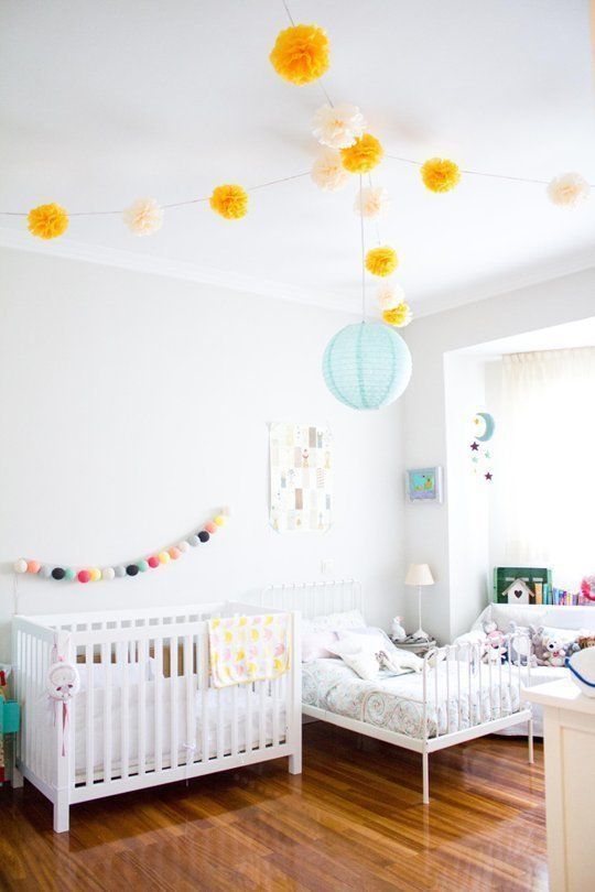 a neutral shared room with colorful lamps, pompom garlands and bright toys and books
