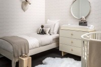 a neutral nursery with matching beds, a simple changing table, printed wallpaper and a faux fur rug
