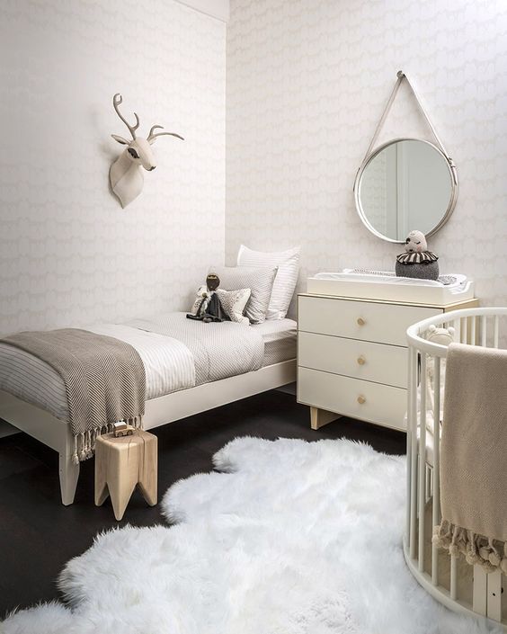 a neutral nursery with matching beds, a simple changing table, printed wallpaper and a faux fur rug