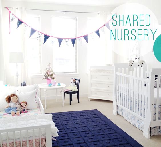 a white shared nursery with touches of navy, a textural rug, a bunting and lots of toys