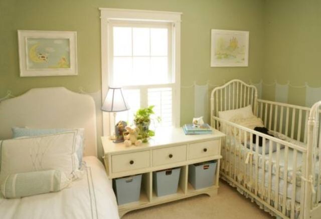 a vintage-inspired green nursery with artworks, elegant beds and a storage unit between them