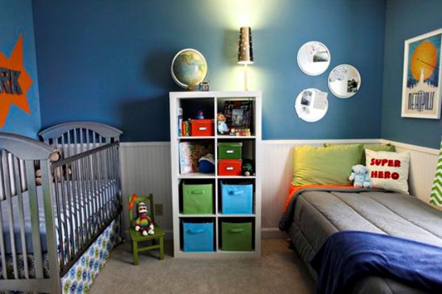 a colorful shared nursery done with a blue wall, colorful textiles and boxes for storage