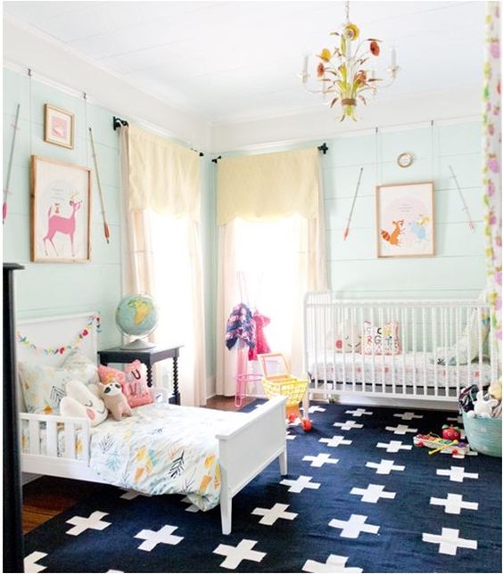 an aqua shared room with yellow curtains, a navy printed rug, bright bedding and artworks