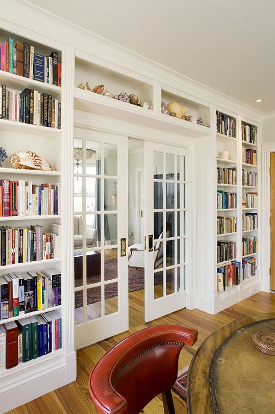 a whole wall taken by lots of open bookshelves on the sides and over the door, with a glass French door is a cool idea to store books and do that with style