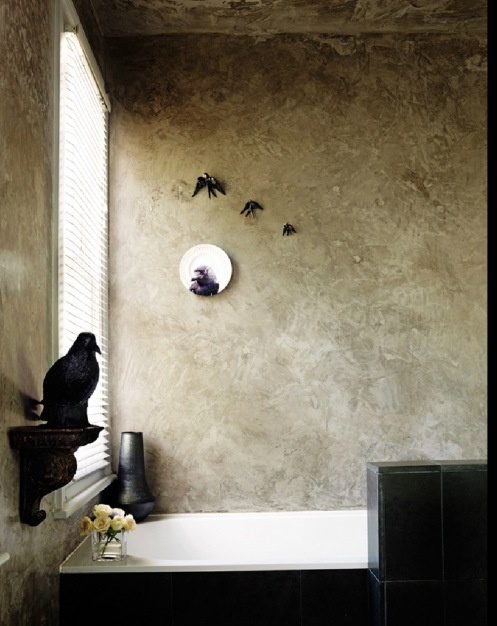 a unique haunted bathroom with neutral textural walls, a black tub and black tiles, black bird decor and a black vase