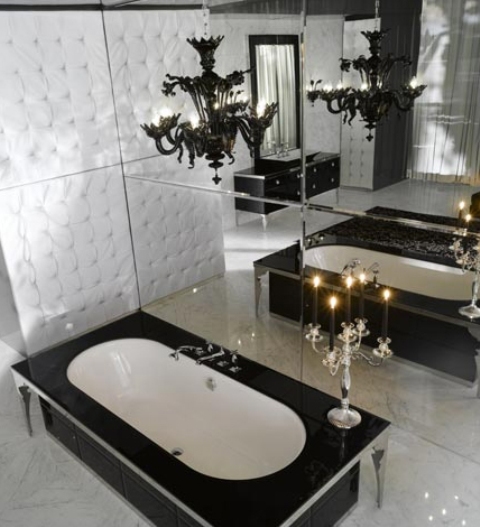 a modern Gothic black and white bathroom with a mirror wall, a tub clad with black tiles, a black chandelier and a vintage candelabra