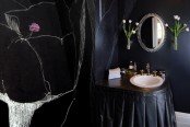 a black Gothic bathroom with black walls, a vanity with a pleated skirt and a white sink, vintage fixtures and floral arrangements is a lovely idea