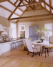 a white and neutral vintage barn kitchen with white cabinets and black countertops, a chalk paint buffet, a round table and mismatching chairs plus wooden beams on the ceiling