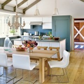 a welcoming barn kitchen with wooden beams on the ceiling, stone blue cabinets and a white kitchen island. a stylish modern farmhouse dining space with a wooden table