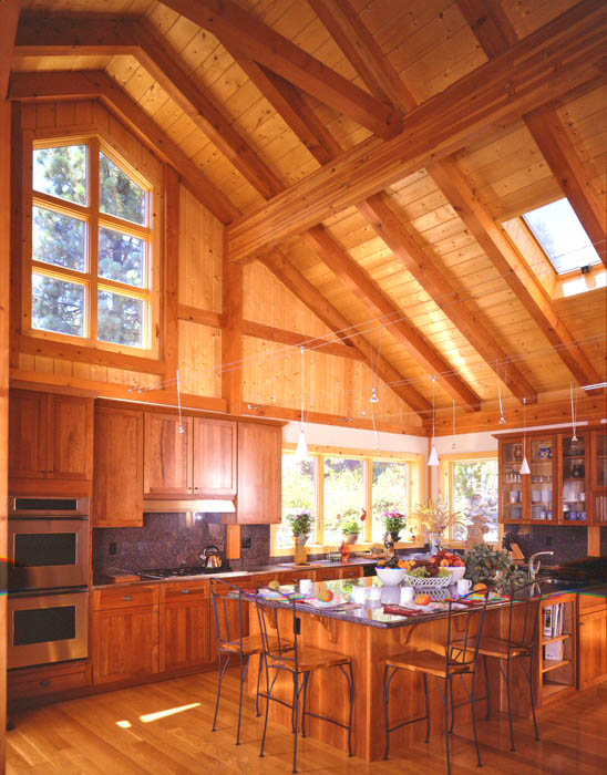 a light stained wood clad kitchen with windows and skylights, with stained shaker style cabinets, a wooden kitchen island and black metal stools