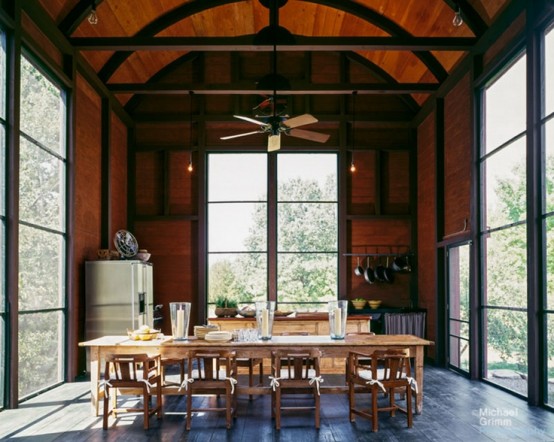 a modern barn kitchen with glazed walls and an arched ceiling, stained cabinetry, a dining space with wooden furniture