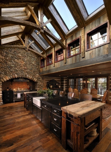 a dark-stained kitchen with a stone accent wall, a ceiling with skylights and rich and dark-stained wooden furniture plus a black kitchen island