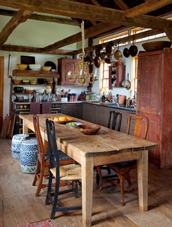 a vintage barn kitchen with wooden beams, vintage shabby chic cabinets, pans hanging on the beams and a wooden dining set