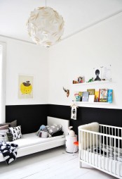 a small Nordic kid’s room with color block walls, a bed and a crib, open shelves, lots of printed pillows and various books and toys