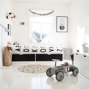 a Nordic kid’s room with a black bed, black and white bedding, artwork, a white dresser for storage and a fabric basket for storing things