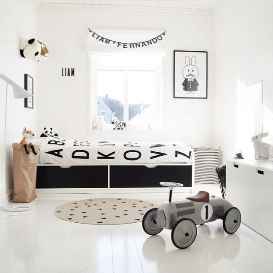 a Nordic kid's room with a black bed, black and white bedding, artwork, a white dresser for storage and a fabric basket for storing things