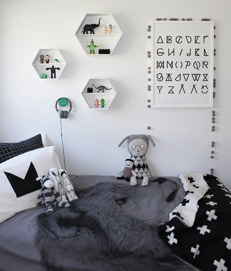 a Scandinavian kid's room with a bed, monochromatic bedding, hexagon shaped shelves and toys and art that match the space color scheme