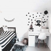a black and white Nordic kid’s room with a black bed and striped bedding, a white desk and a chair, a polka dot accent and some artwork
