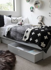 a Nordic kid’s room with white hexagon shelves, a white bed with monochromatic bedding, layered rugs and some pretty toys is a welcoming space for kids