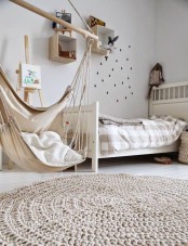 a neutral and welcoming kid’s room with a Scandinavian design, light-stained box shelves, a light-stained bed with neutral bedding, a pendant chair and a rug