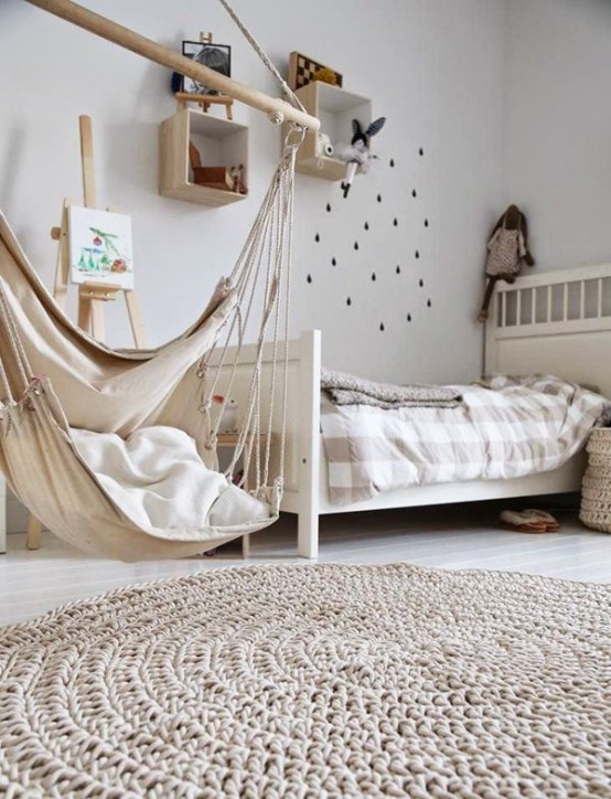 a neutral and welcoming kid's room with a Scandinavian design, light-stained box shelves, a light-stained bed with neutral bedding, a pendant chair and a rug