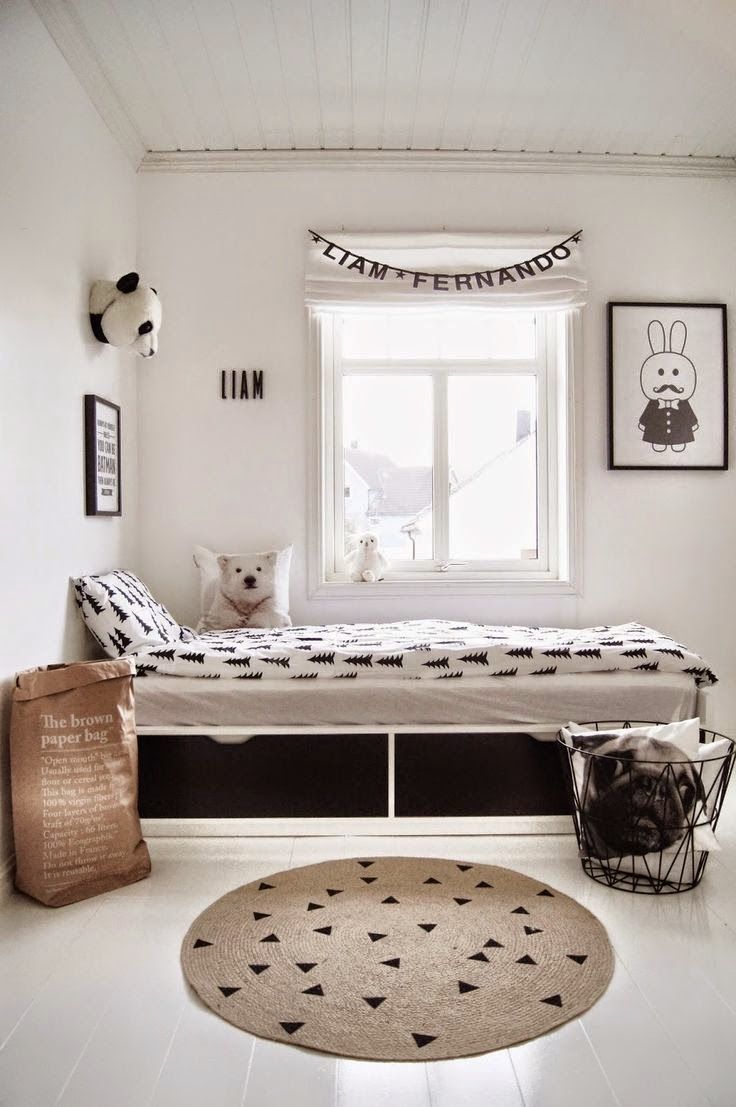 a black and white Scandinavian kid's room with a white storage bed with black and white bedding, a jute rug and a metal basket for storage, black and white artwork and much natural light