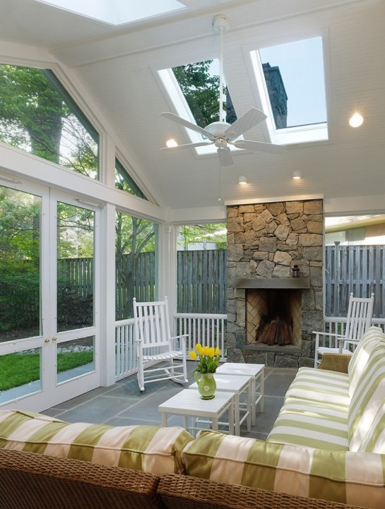 a cozy rustic attic sunroom with plaid furniture, a stone clad fireplace, some lights and a pendant fan