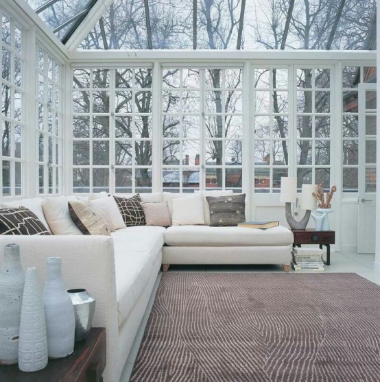 a neutral contemporary sunroom with stylish furniture, dark tables with vases and all the glazed walls and a ceiling