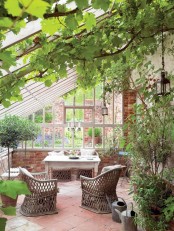 a lovely vintage sunroom with a tiled floor and brick walls, vintage furniture including rattan chairs and potted greenery everywhere