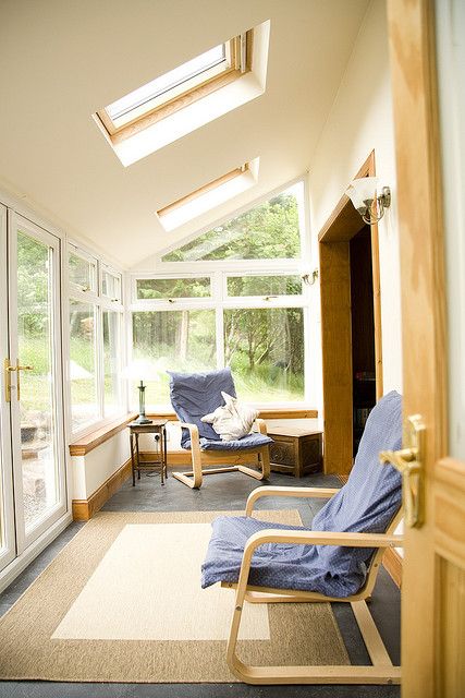 a neutral ultra-modern sunroom space with layered rugs, blue chairs and cool skylights to get more natural light