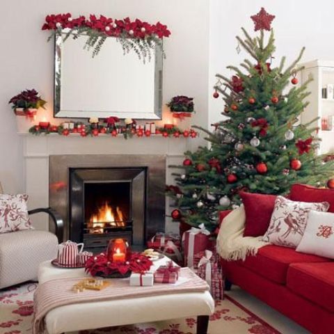 a red and white Christmas living room with a bold decorated tree, holiday pillows, red ornaments and candles on the mantel and some bold poinsettia blooms on the mirror
