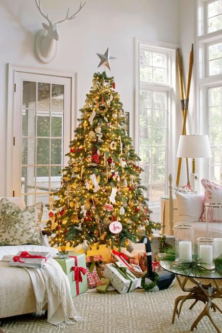 a Christmas tree with lights, red and white ornaments and some gifts under it is very bright and sets the tone in the space