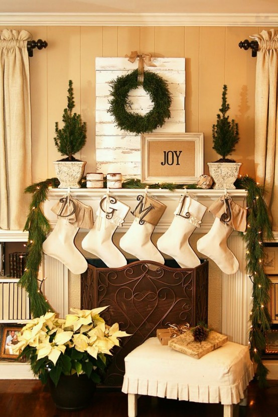 a neutral space with a fir garland, a greenery wreath, stockings, lights and mini potted trees is very chic and cool