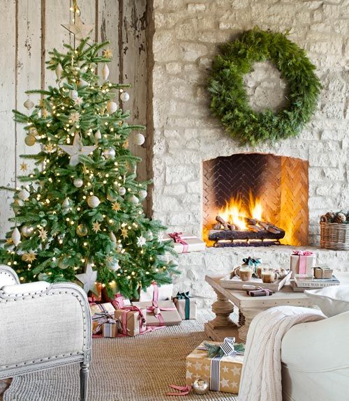 a neutral French farmhouse living room with a fir wreath over the hearth, a Christmas tree with metallic and white ornaments, gifts that create a holiday mood