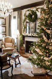 an evergreen wreath, lots of candles and ornaments on the mantel and a Christmas tree decorated with lights, gold ornaments and burlap ribbons for a festive feel in the space
