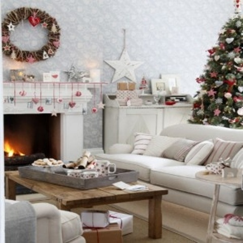 a neutral living room accented with red and white ornaments hung to the mantel, with a vine wreath with ornaments and a Christmas tree decorated with them